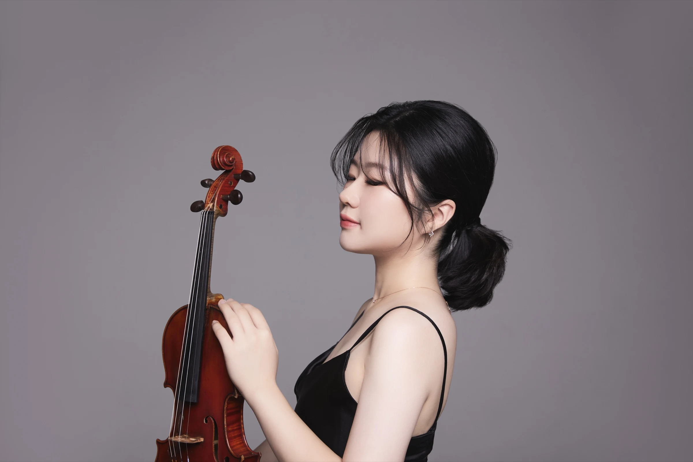 Profile portrait of Byeol Kim in a black dress with her violin