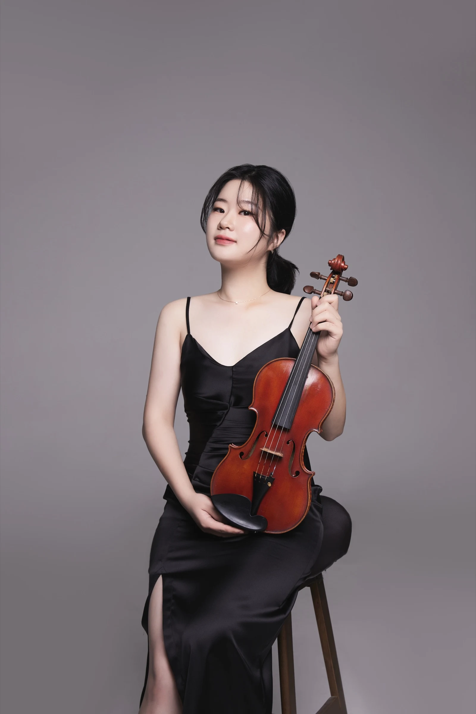 Seated portrait of Byeol Kim in a black dress holding her violin